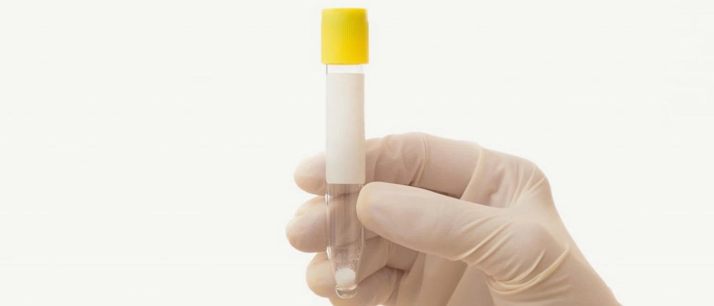Gloved hand holding a labelled sample collection tube